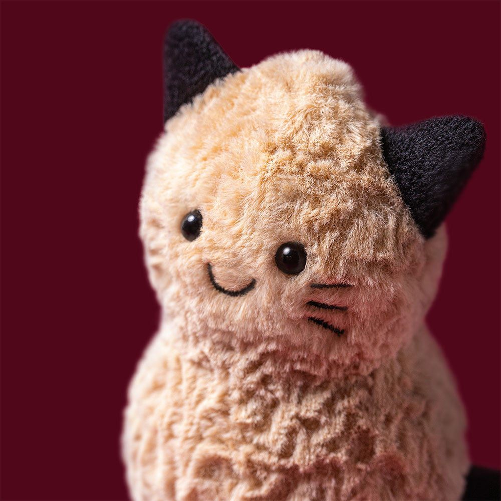 Detailansicht vom Lachgesicht mit schwarzen Katzenohren und den aufgemalten schwarzen Katzenhaaren des Jellycat Amuseables Peanut Cat