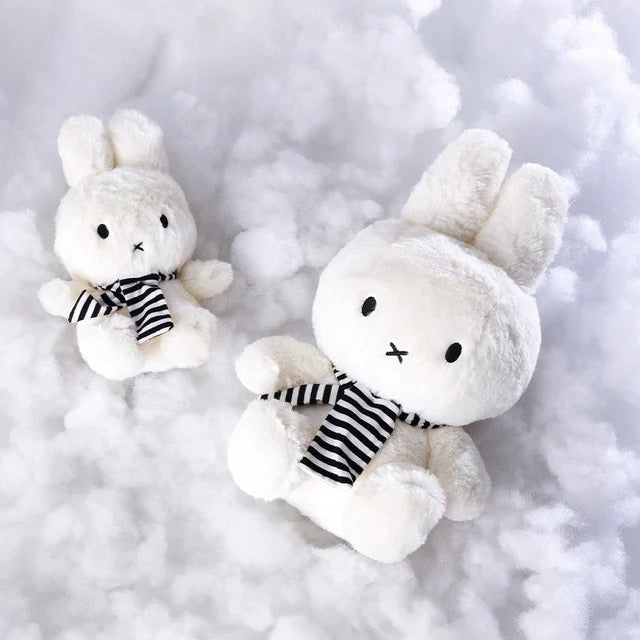 Zwei weiße Miffy with Scarf Plüschfiguren mit gestreiftem Schal liegen auf weicher Füllwatte