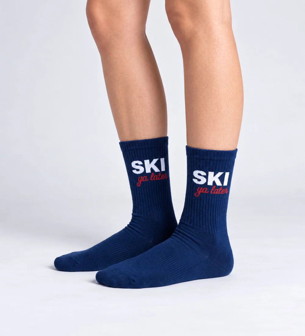 Dunkelblaue Unisex-Socken Ski ya later von No Bad Days Club mit weißem und rotem Schriftzug, an den Füßen getragen.