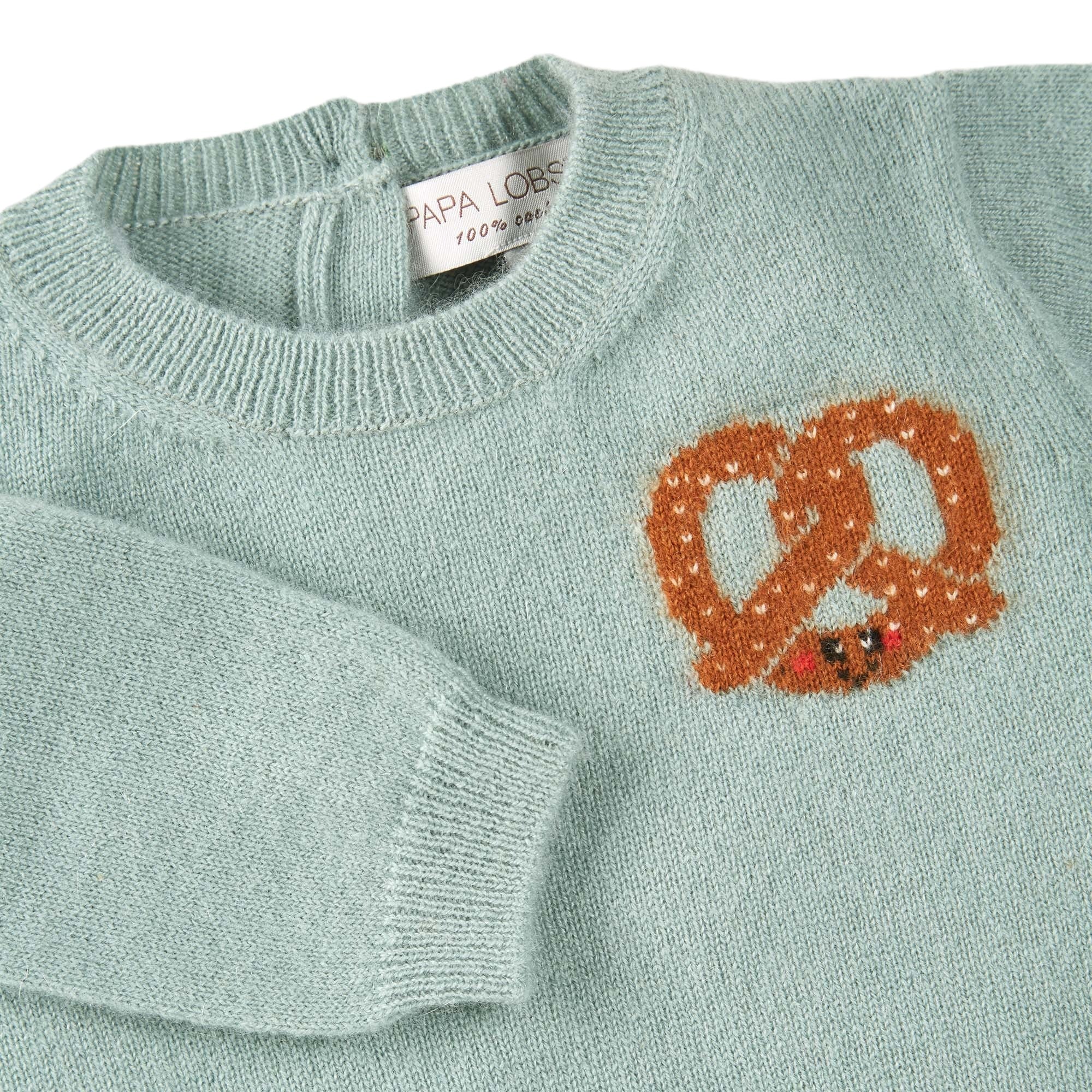 Detailansicht: Kaschmirpullover Brezel von PAPA LOBSTER in Salbei mit kleiner Brezel auf der Brust für Babys und Kinder