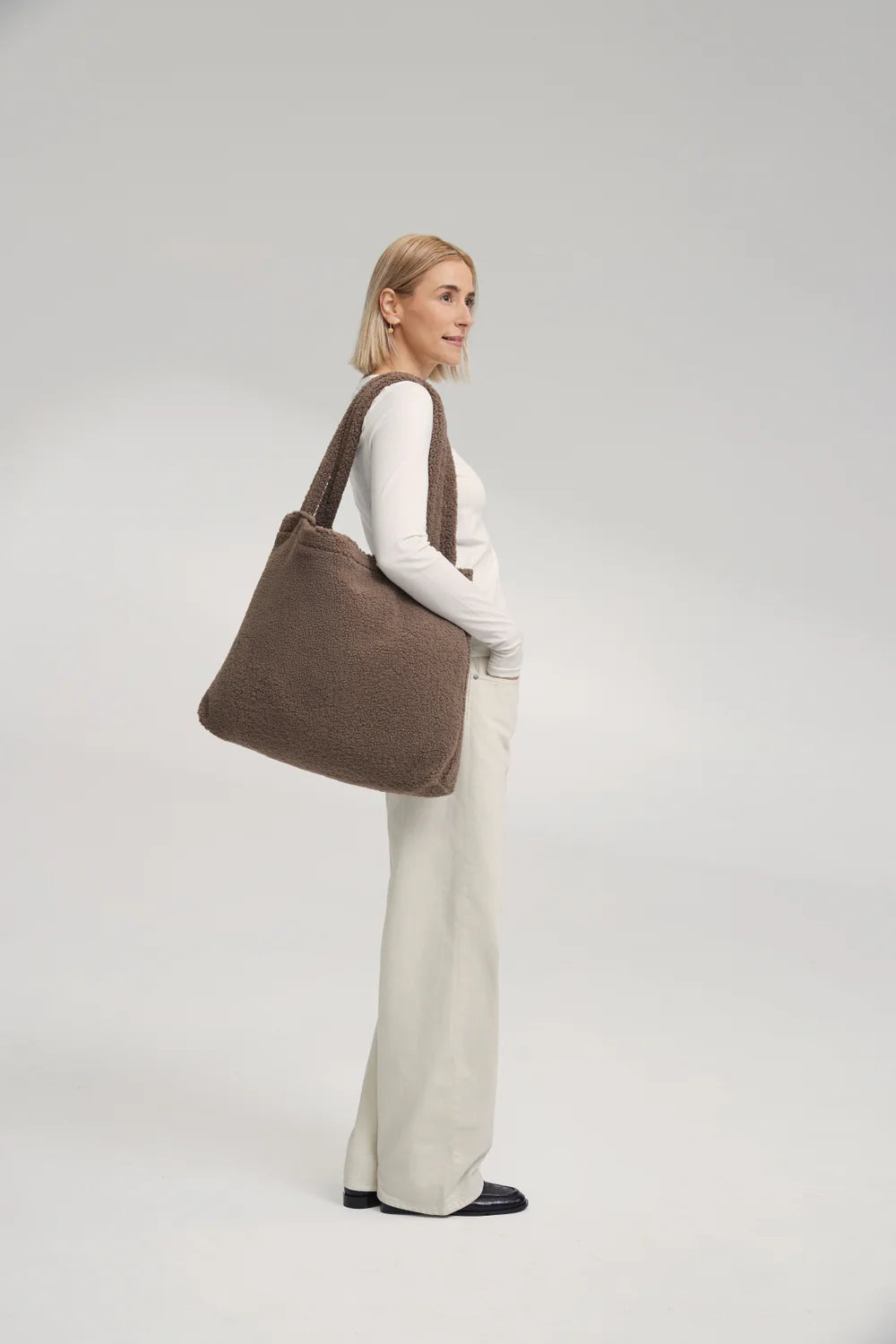 Foto: Frau trägt die Studio Noos Teddy Mom-Bag l Braun aus weichem braunem Teddy-Stoff mit breiten Henkeln lässig über der Schulter