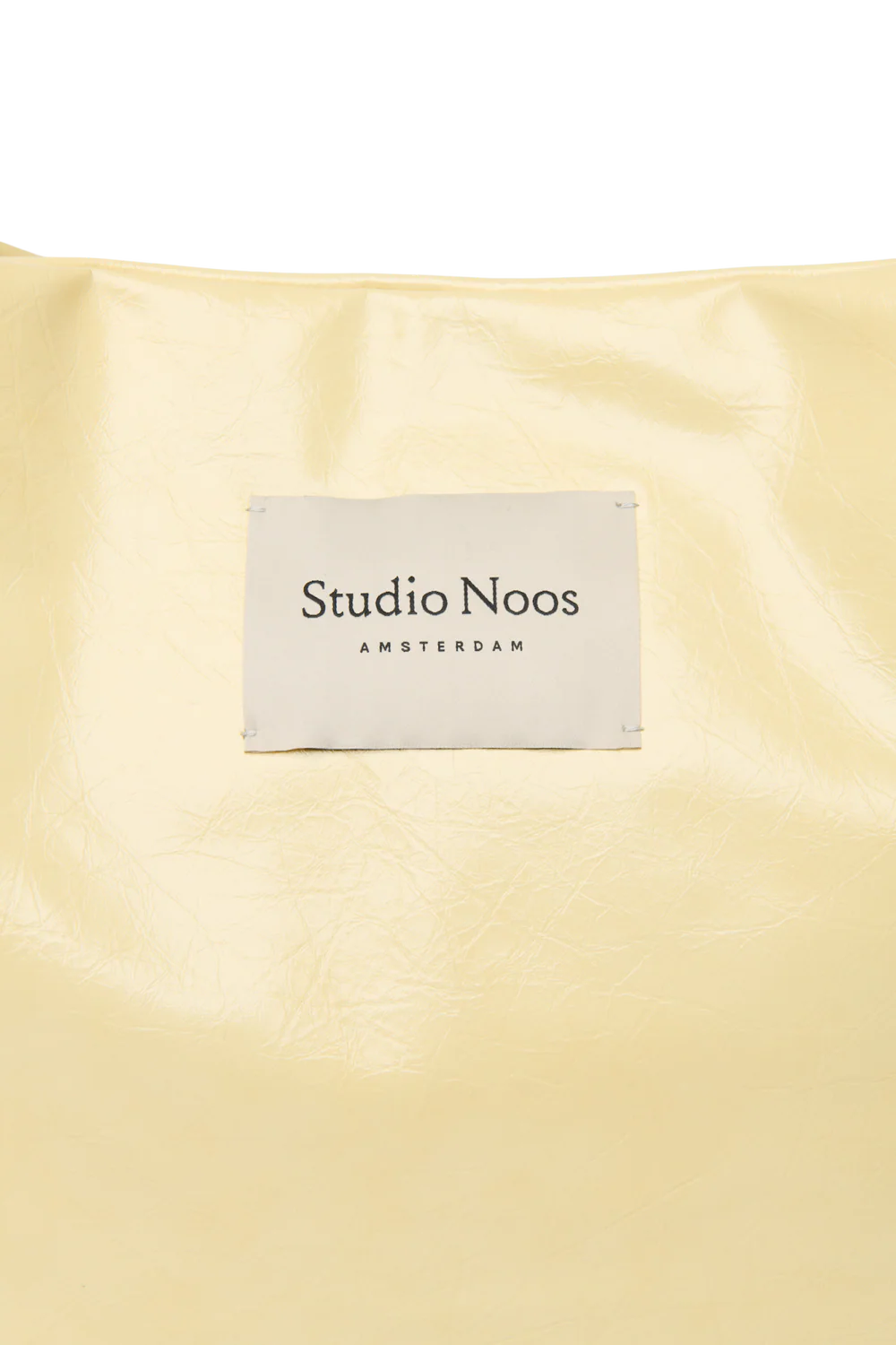 Detailansicht: Studio Noos Vegan Leather Mom Bag in Buttergelb mit gepolsterten Griffen und kleinem Studio Noos Amsterdam Label vorne