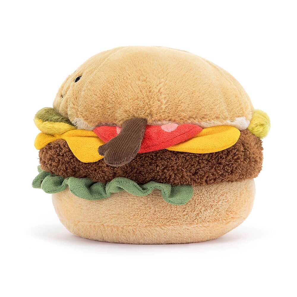 Seitnansicht: Jellycat Amuseables Burger – sitzendes Burger-Kuscheltier mit Brötchen, Salat, Käse, Burger-Patty, Tomate, Gurke, braunen Füßchen und lachendem Gesicht mit schwarzen Knopfaugen.