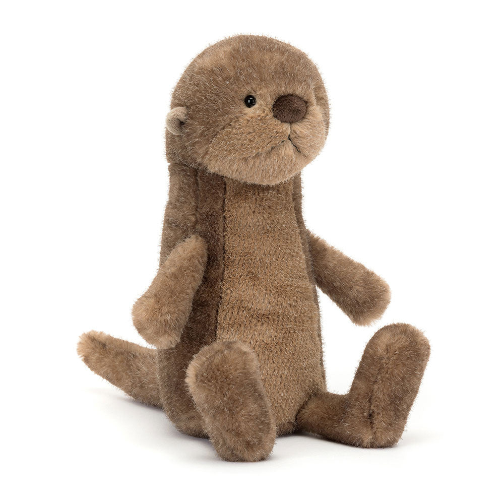 Braunes Jellycat Brooke Otter Kuscheltier sitzt kerzengerade am Ufer und schaut aufmerksam in die Umgebung, wirkt wie ein kleiner Wächter der Flusslandschaft