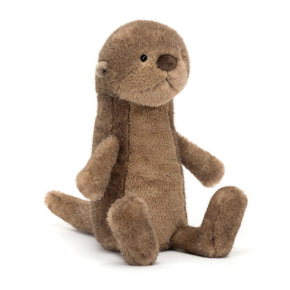 Braunes Jellycat Brooke Otter Kuscheltier sitzt kerzengerade am Ufer und schaut aufmerksam in die Umgebung, wirkt wie ein kleiner Wächter der Flusslandschaft