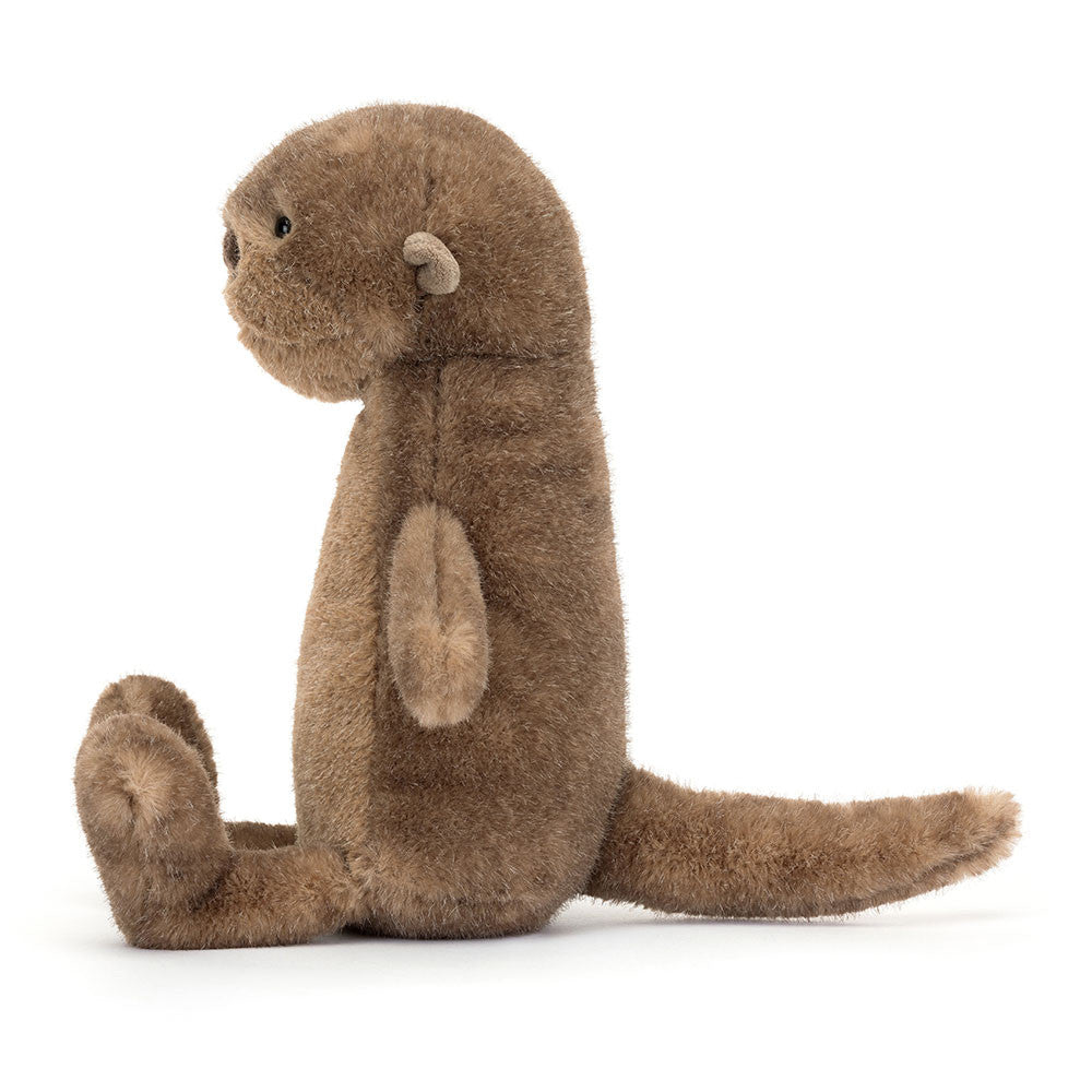 Braunes Jellycat Brooke Otter Kuscheltier sitzt kerzengerade am Ufer und schaut aufmerksam in die Umgebung, wirkt wie ein kleiner Wächter der Flusslandschaft