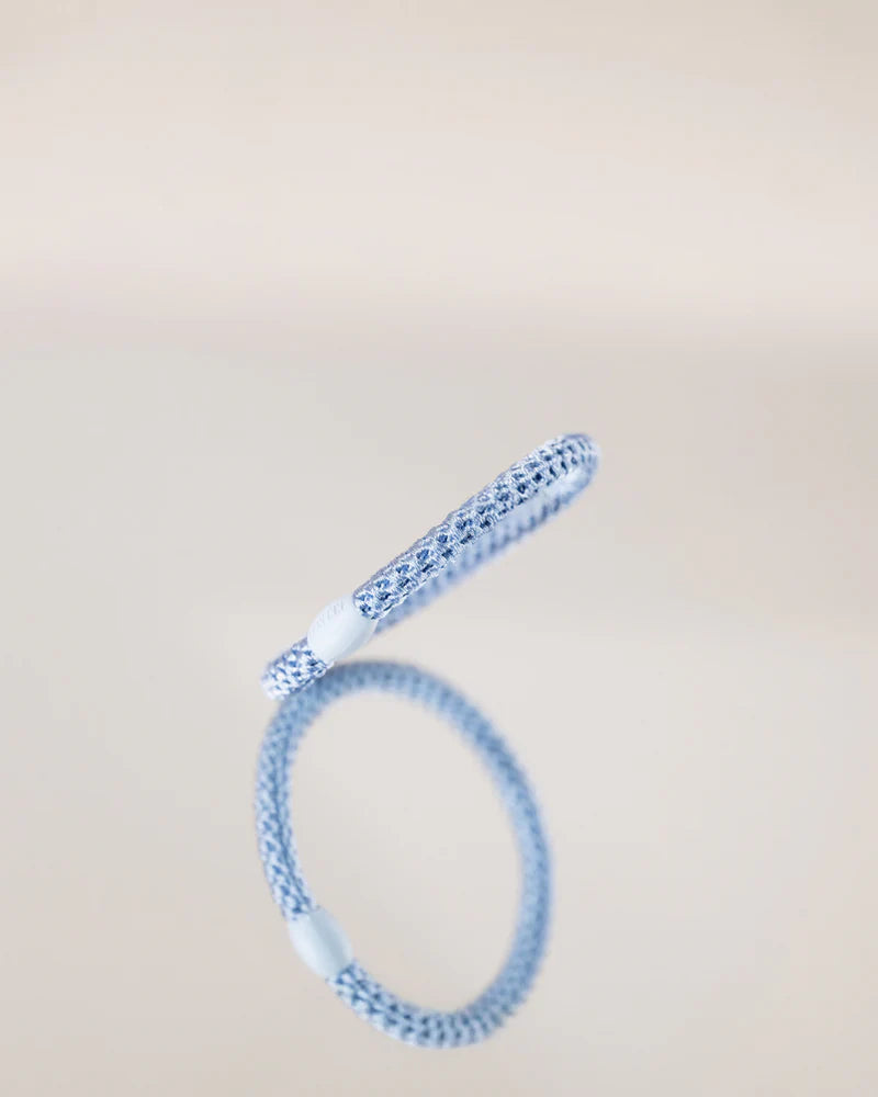 KKNEKKI Haargummi SLIM – Sky Blue, hellblaues Haargummi auf einem Spiegel liegend