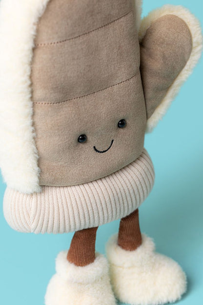 Jellycat Amuseables Fitswell Mitten Fäustling in Beige, stehend mit kleinen Füßen in Winterboots, flauschigem Rand und lachendem Gesicht von vorne