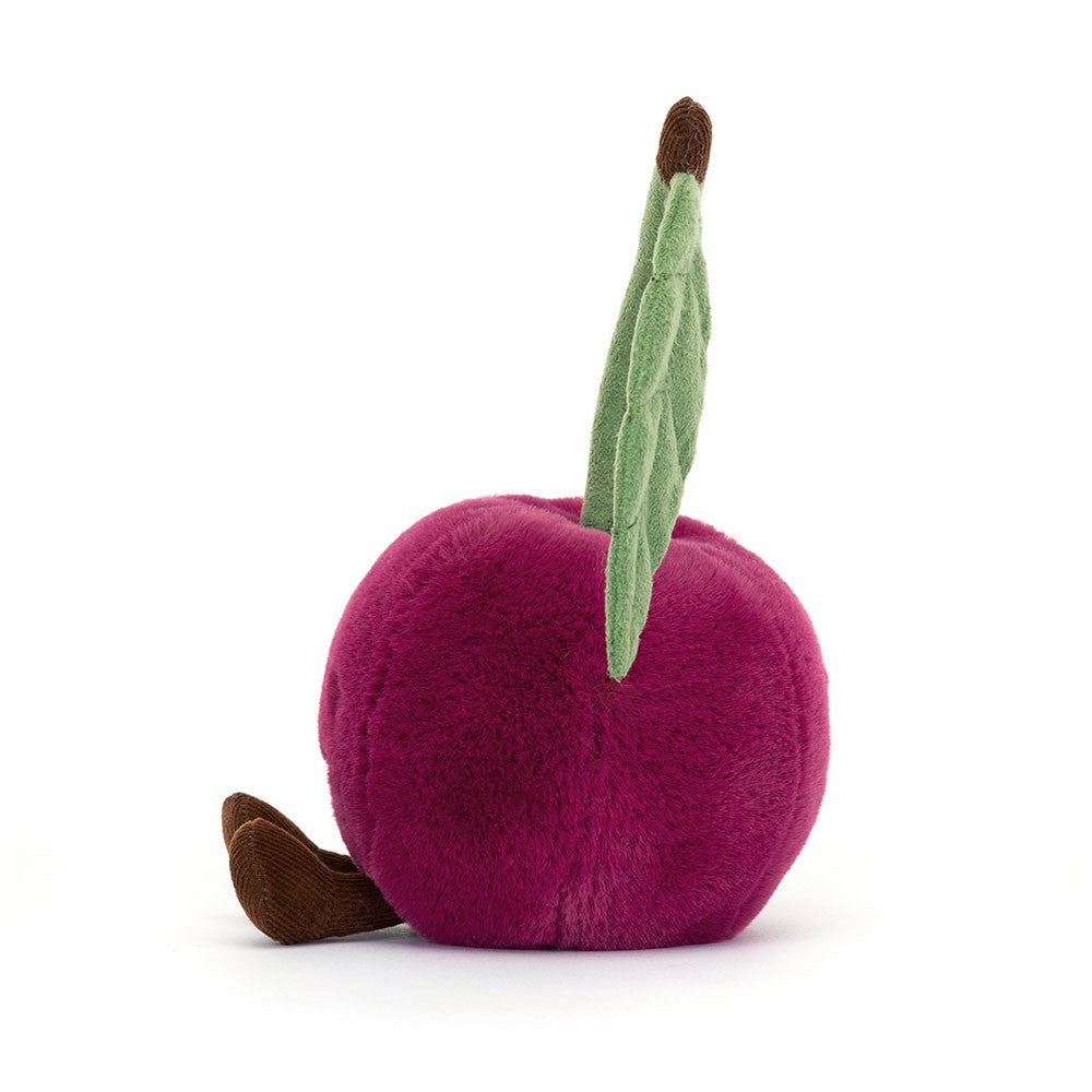 Seitenansicht: Jellycat Amuseables Cherry Plüschkirsche in dunklem Kirschrot mit Stiel, grünem Blatt, lachendem Gesicht und ausgestreckten Füßen