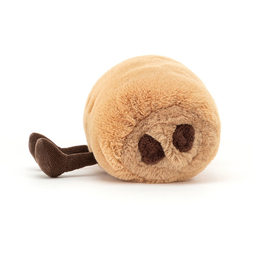 Seitenansicht: Jellycat Amuseables Pain au Chocolate – hellbraunes Croissant-Kuscheltier mit lachendem Gesicht, schwarzen Knopfaugen und ausgestreckten braunen Füßchen.