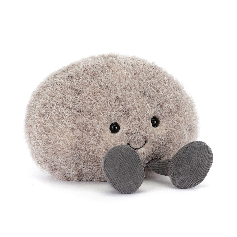 Jellycat Amuseables Pebble sitzt entspannt mit ausgestreckten Füßen und sanftem Lächeln – ein ruhiger, kleiner Kuschelbegleiter