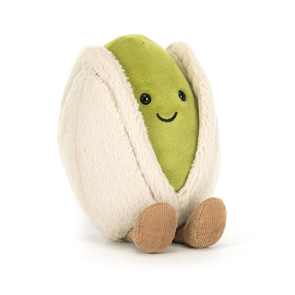 Vorderansicht Jellycat Amuseables Pistachio – sitzende grüne Plüsch-Pistazie mit lachendem Gesicht und schwarzen Knopfaugen, die aus einer hellbeigen Hülle schaut und hellbraune Füßchen hat.
