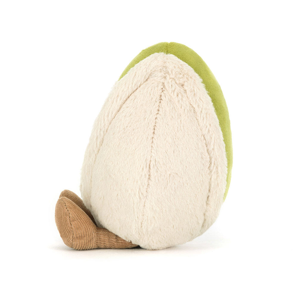 Seitenansicht Jellycat Amuseables Pistachio – sitzende grüne Plüsch-Pistazie mit lachendem Gesicht und schwarzen Knopfaugen, die aus einer hellbeigen Hülle schaut und hellbraune Füßchen hat.