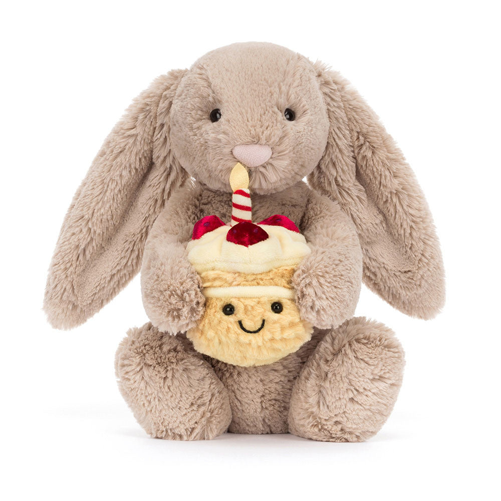Vorderansicht: Jellycat Bashful Beige Bunny Birthday – sitzender beiger Kuscheltier-Hase mit Hängeohren und kleinem Geburtstagskuchen und Kerze in den Pfoten.