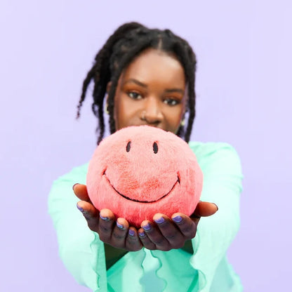 Frau hält Smiley ECO Fuzzy Plüsch-Smiley in der Farbe Coral, 13 cm, von Bon Ton Toys in den Händen
