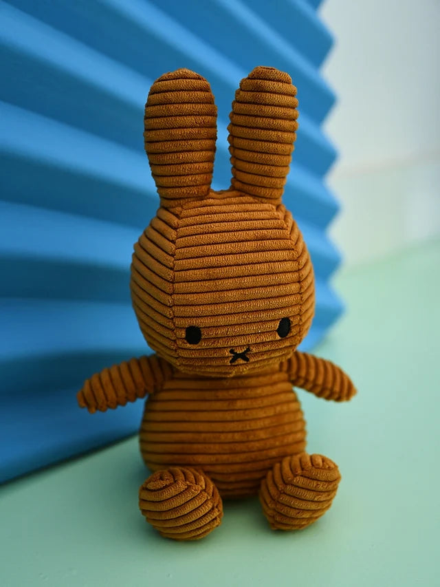 Miffy Hase aus braunem Cord in der Farbe Cinnamon sitzt vor einem blau-grünen Hintergrund.