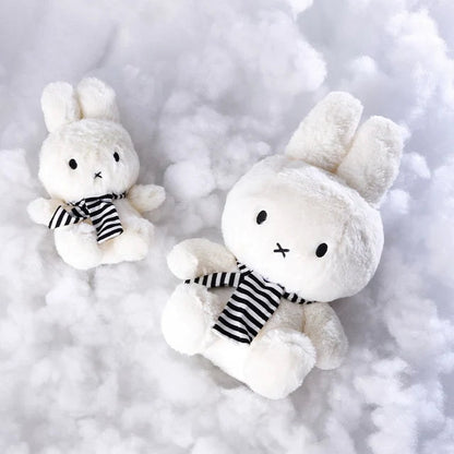 Zwei weiße Miffy with Scarf Plüschfiguren mit gestreiftem Schal liegen auf weicher Füllwatte
