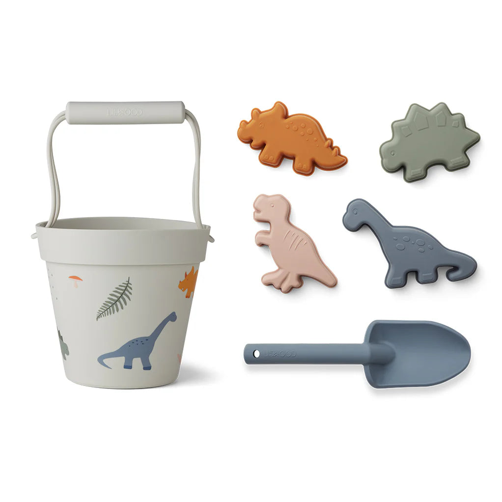 Strandspielzeug Set Dinosaurier von Liewood bestehend aus Eimer, Schaufel und vier Sandförmchen (T-Rex, Brontosaurus, Stegosaurus).