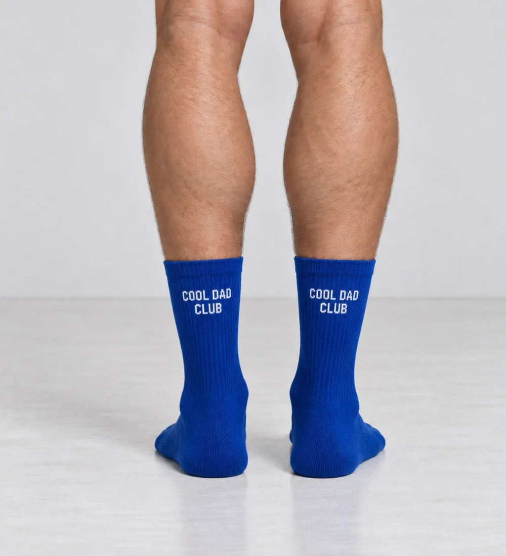 Blaue Herrensocken COOL DAD CLUB von No Bad Days Club mit weißem Schriftzug, an den Füßen getragen.
