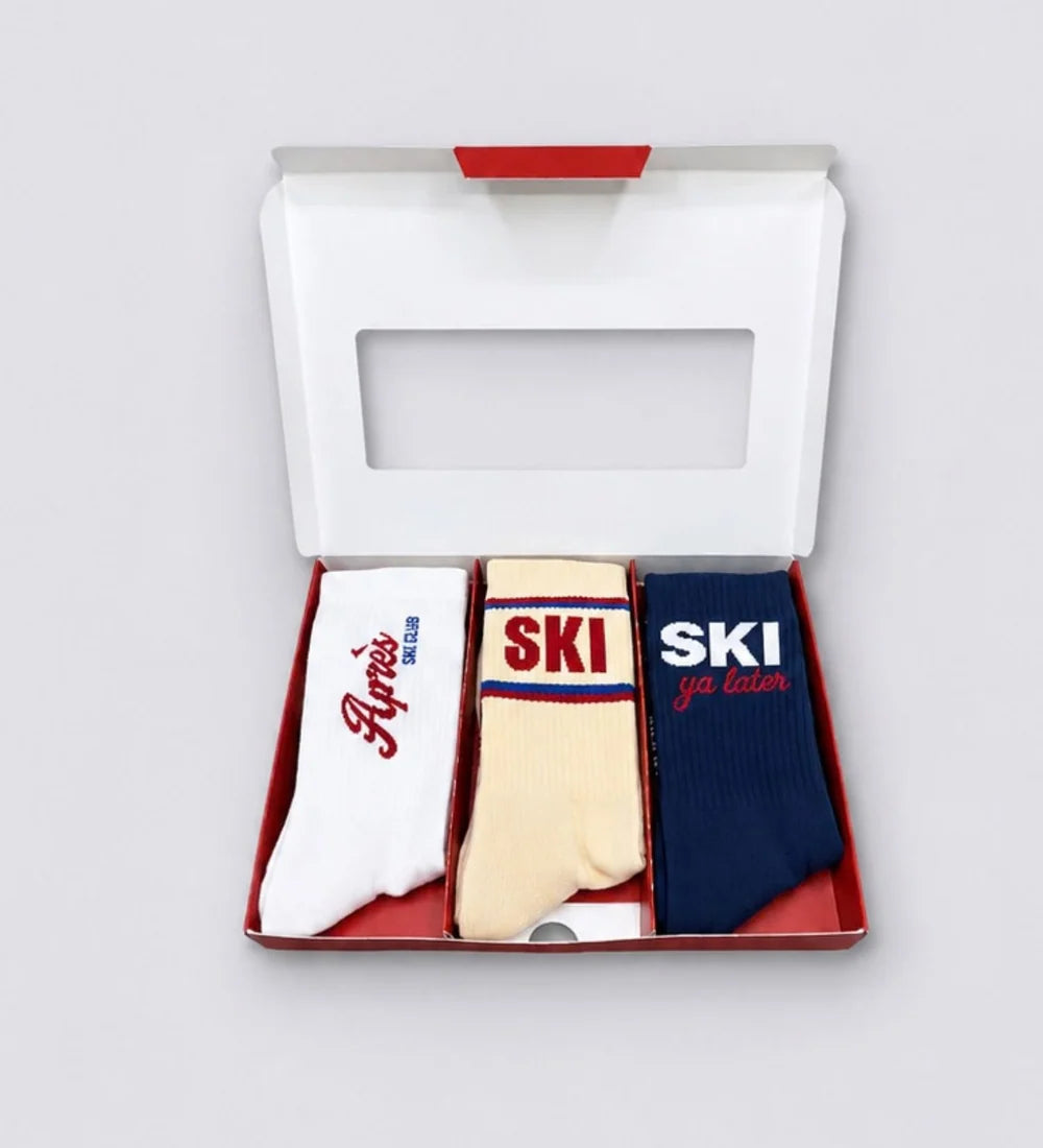 Geöffnete APRÈS SKI Geschenkbox von No Bad Days Club mit drei Paar Socken in Weiß, Creme und Dunkelblau.