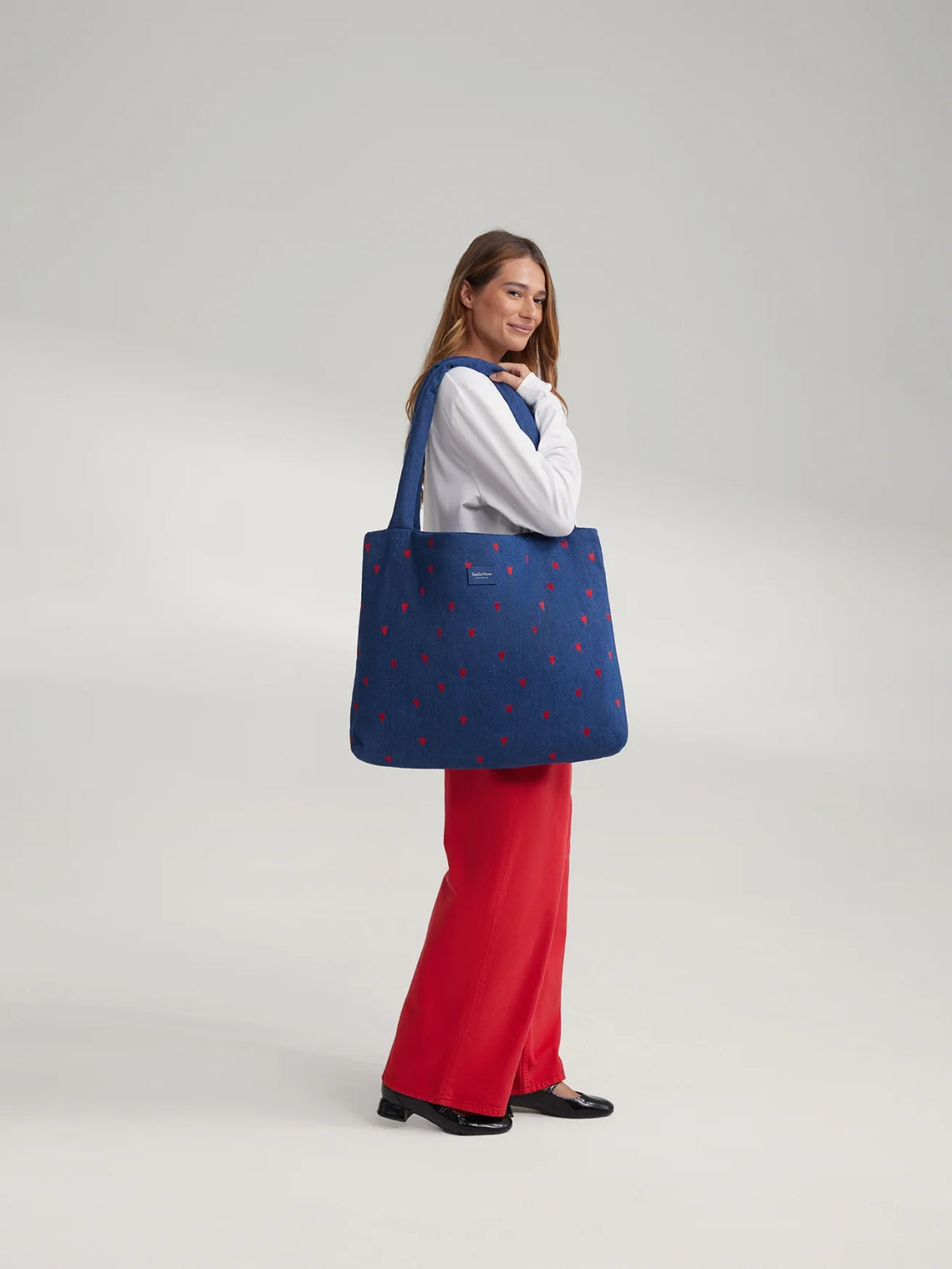 Frau trägt eine Studio Noos Mom-Bag über der Schulter aus dunkelblauem Denim mit wattierten Henkeln, gestickten roten Herzen und Logo