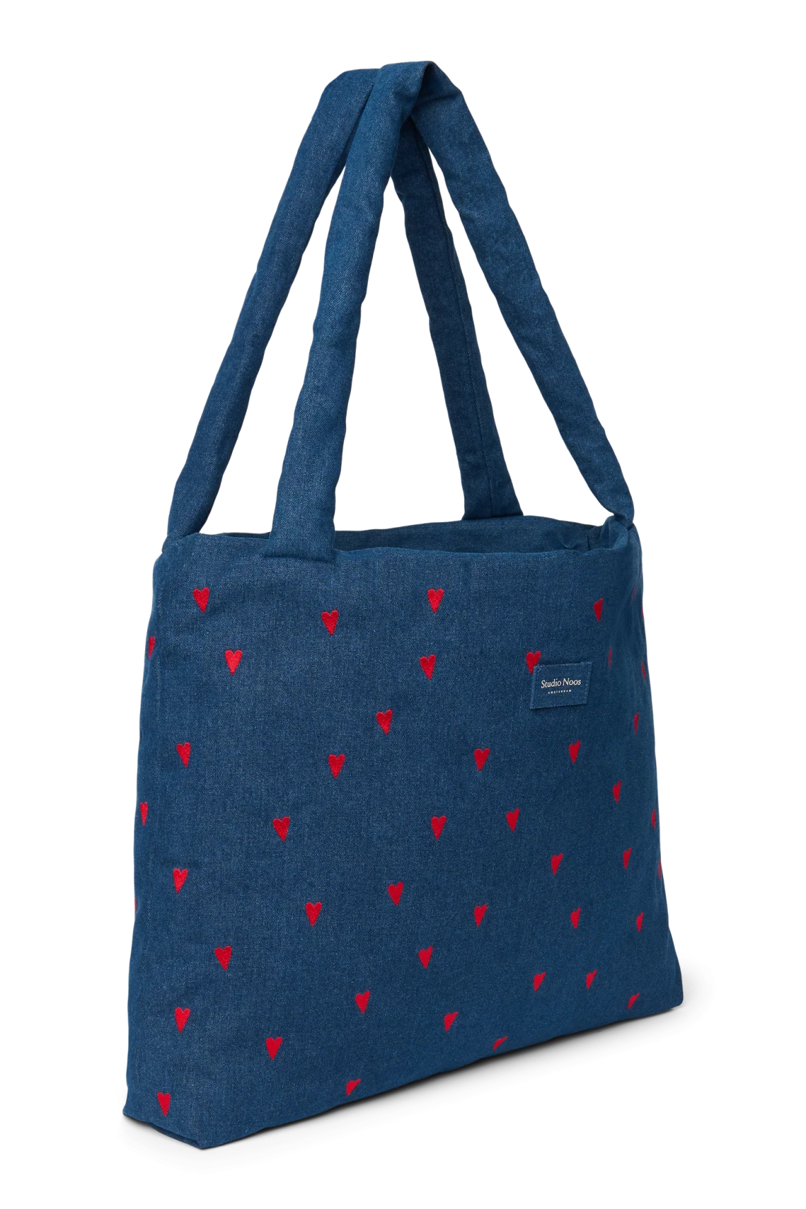 Schräge Ansicht der Studio Noos Mom-Bag aus dunkelblauem Denim mit wattierten Henkeln, gestickten roten Herzen und Logo
