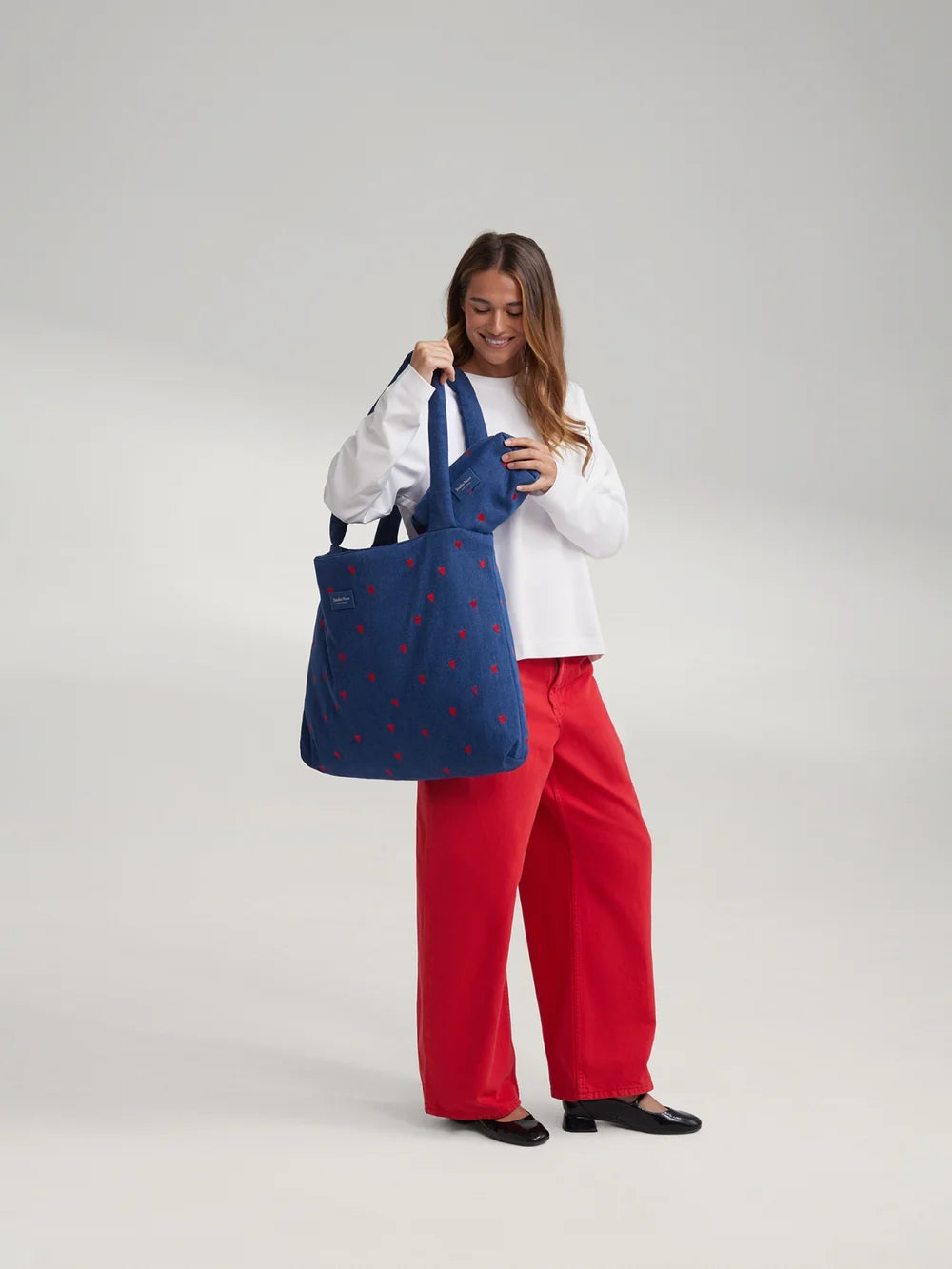 Frau mit Pouch aus dunkelblauem Denim mit gestickten roten Herzen in der Hand