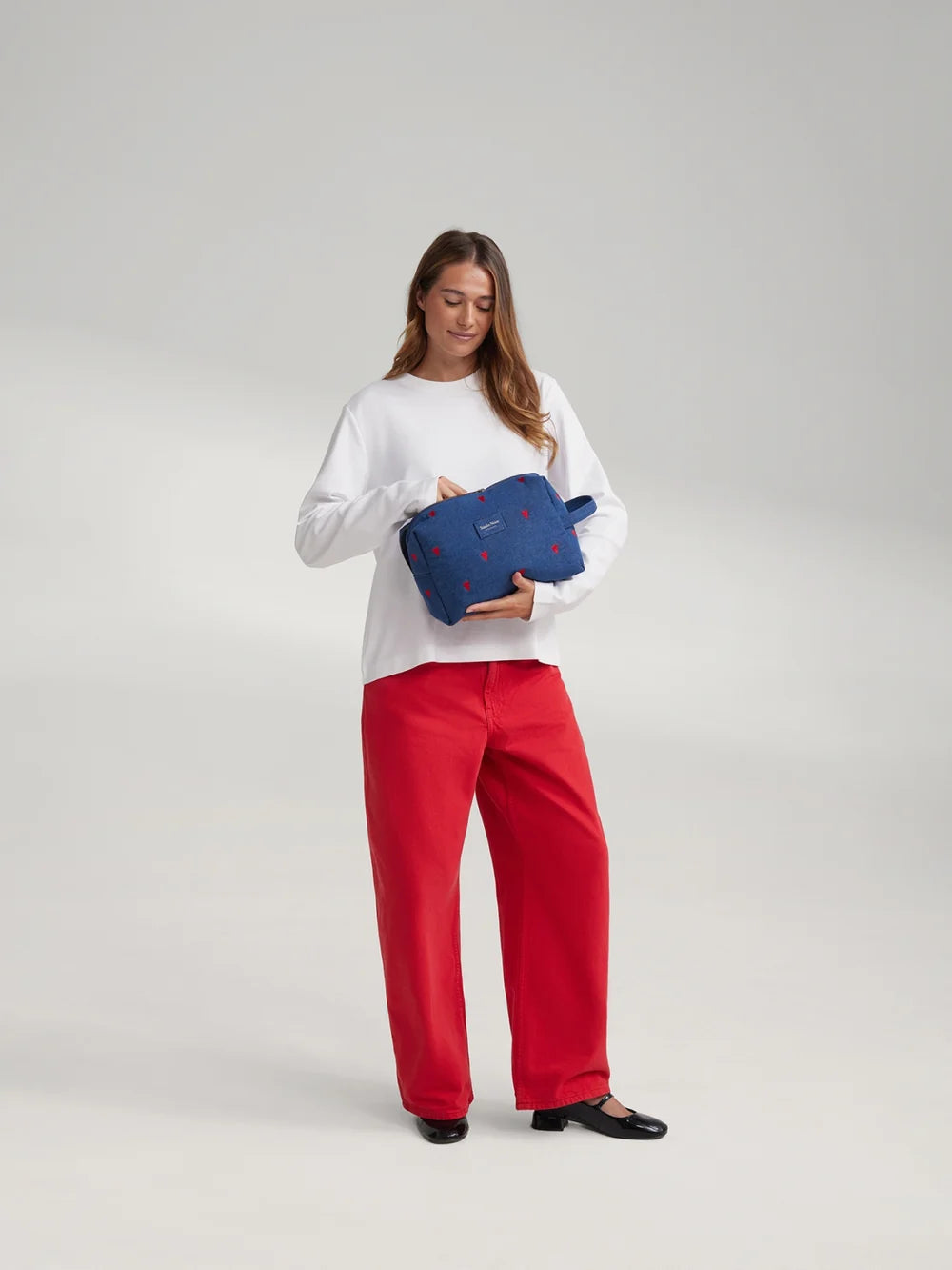 Frau trägt eine dunkelblaue Denim Kosmetiktasche von Studio Noos mit gestickten roten Herzen