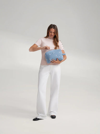 Frau trägt eine hellblaue Denim Kosmetiktasche von Studio Noos mit gestickten Pastell-Herzen