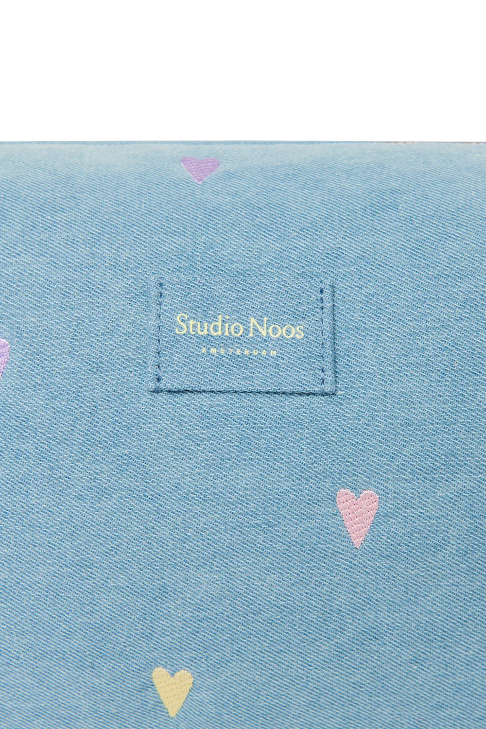 Detailansicht des Studio Noos Logos auf der hellblauen Denim Kosmetiktasche mit gestickten Pastell-Herzen