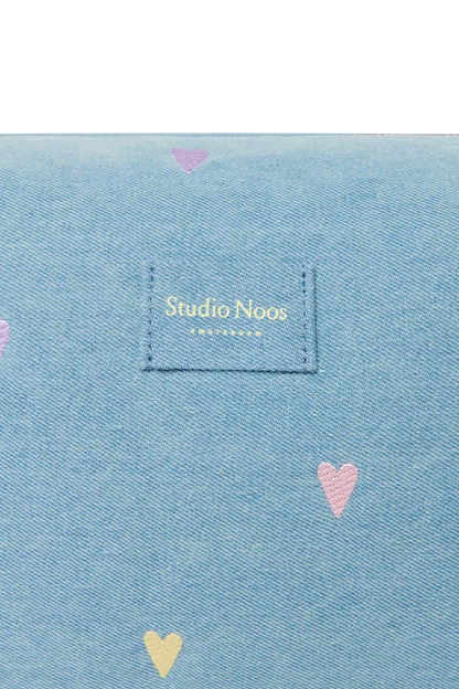 Detailansicht des Studio Noos Logos auf der hellblauen Denim Kosmetiktasche mit gestickten Pastell-Herzen