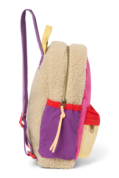 Seitenansicht: Studio Noos Patchwork Mini-Rucksack l Bright Pink mit Reissverschluss-Mesh-Tasche vorne und seitlichen Taschen. In bunten Farben mit beigem Teddy-Stoff, Patchwork-Details mit pink-rot-lila-beigen Akzenten. Lila Träger verstellbar und an der Rückseite ausschließlich beiger Teddystoff.