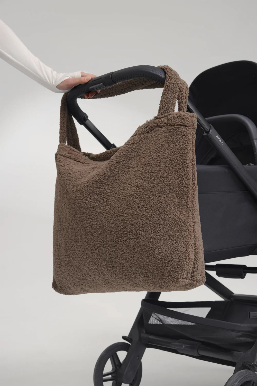 Foto: Studio Noos Teddy Mom-Bag l Braun aus weichem braunem Teddy-Stoff mit breiten Henkeln hängt über einem Kinderwagen-Griff