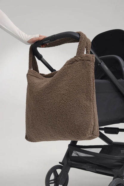 Foto: Studio Noos Teddy Mom-Bag l Braun aus weichem braunem Teddy-Stoff mit breiten Henkeln hängt über einem Kinderwagen-Griff
