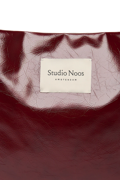 Detailansicht: Vorderansicht: Studio Noos Vegan Leather Mom Bag in Bordeauxrot mit gepolsterten Griffen und kleinem Studio Noos Amsterdam Label vorne
