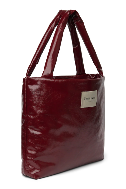 Seitenansicht: Studio Noos Vegan Leather Mom Bag in Bordeauxrot mit gepolsterten Griffen und kleinem Studio Noos Amsterdam Label vorne