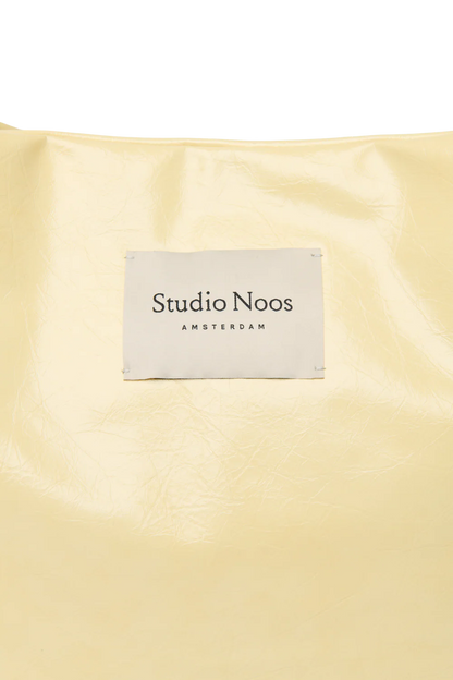 Detailansicht: Studio Noos Vegan Leather Mom Bag in Buttergelb mit gepolsterten Griffen und kleinem Studio Noos Amsterdam Label vorne