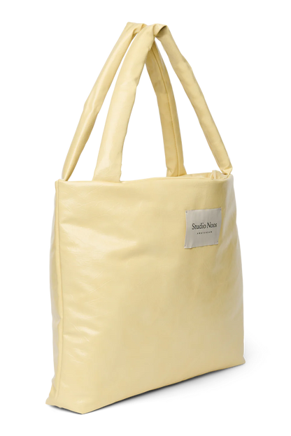 Seitenansicht: Studio Noos Vegan Leather Mom Bag in Buttergelb mit gepolsterten Griffen und kleinem Studio Noos Amsterdam Label vorne